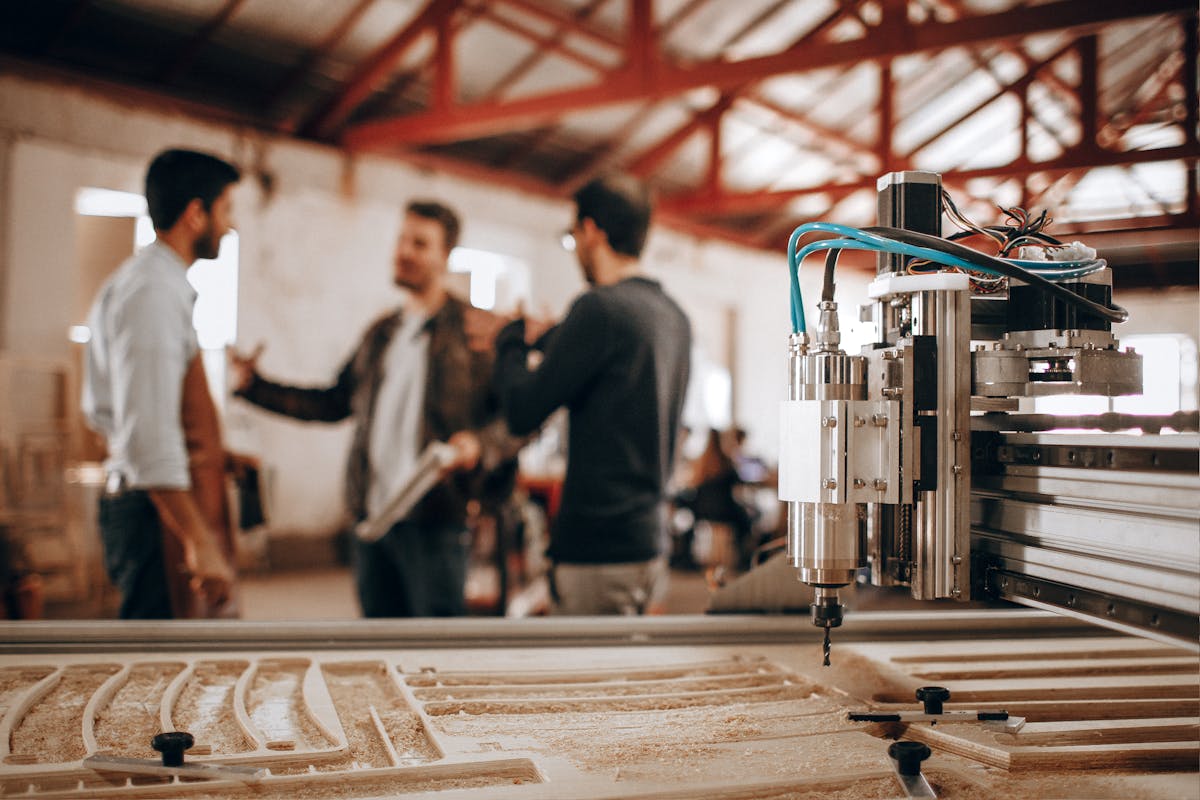 Equipo de carpinteros discutiendo diseños junto a máquina CNC en taller moderno